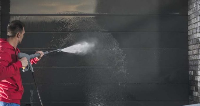 homme nettoyant porte de garage au nettoyeur haute pression.
