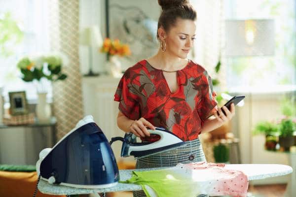 femme qui regarde son téléphone en repassant