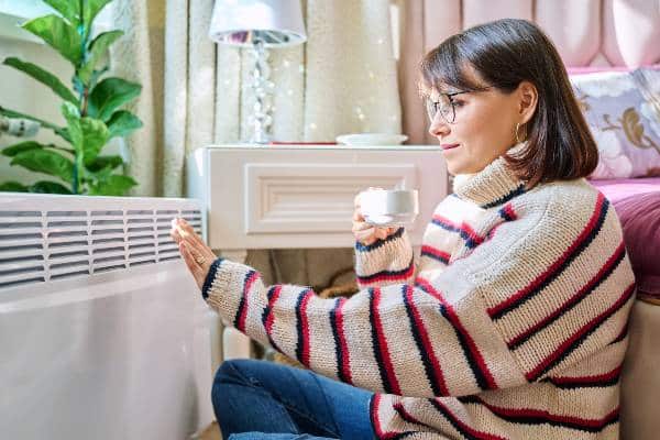 jeune femme se réchauffant près d'un radiateur