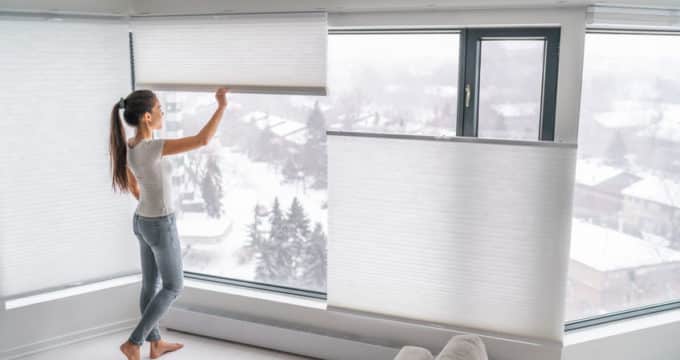 woman opening home curtains in urban condo. modern top down bottom up privacy cellular shades on apartment window keeping heat in winter with honeycomb blind curtain. cordless pleated shades.