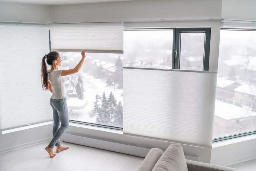 woman opening home curtains in urban condo. modern top down bottom up privacy cellular shades on apartment window keeping heat in winter with honeycomb blind curtain. cordless pleated shades.