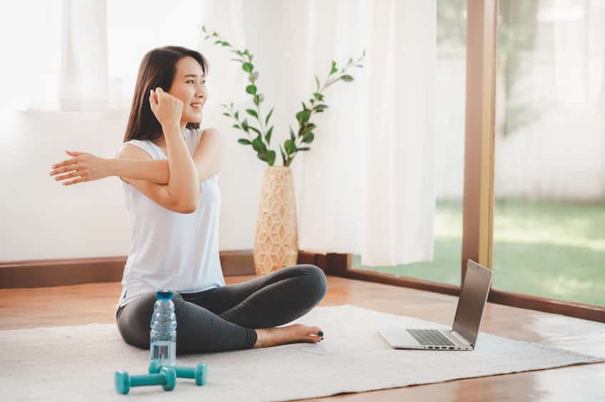 asian woman doing yoga shoulder stretching online class at home